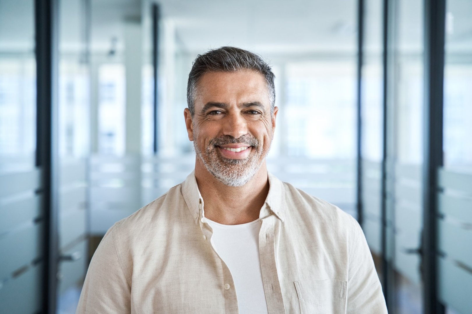 Headshot close up portrait of indian or latin confident mature good looking middle age leader, ceo male businessman on blur office background. Handsome hispanic senior business man smiling at camera.